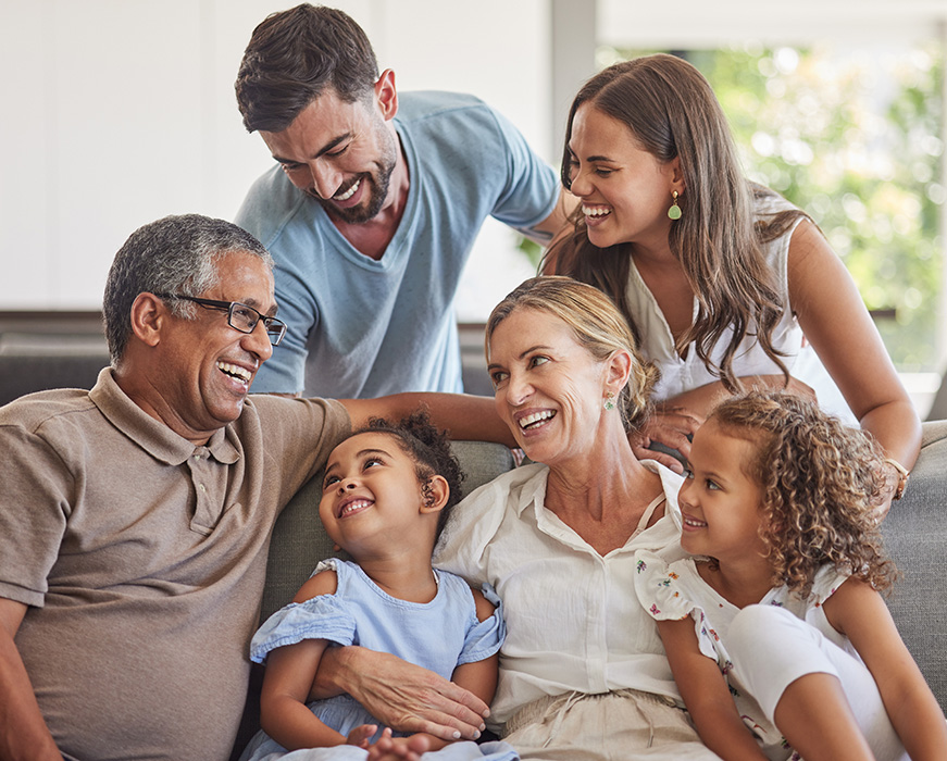 The image shows a family gathered on a couch, with adults smiling at the camera and a child being held by an adult, all appearing happy and close together.