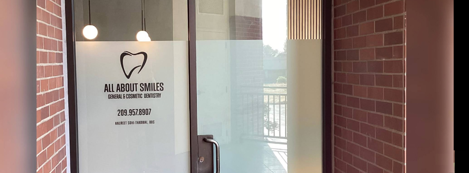 The image shows an interior space with a sign that reads  ALL ABOUT SMILES  on a brick wall, and there s a glass door with a heart symbol above it.