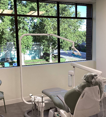The image shows a modern dental office interior with a dental chair, treatment table, and equipment.