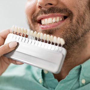 The image shows a person holding a dental device with multiple toothbrush heads, smiling at the camera while looking into a mirror.