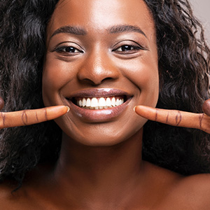 A woman with a big smile, holding up two fingers on each hand, showcasing her teeth.
